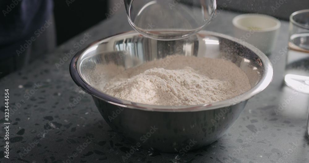 pour flour into steel bowl on concrete countertop