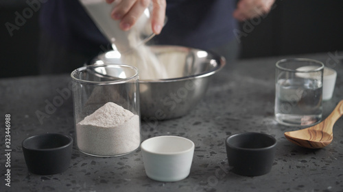 man adds dry ingredients into flour in steel bowl on concrete countertop