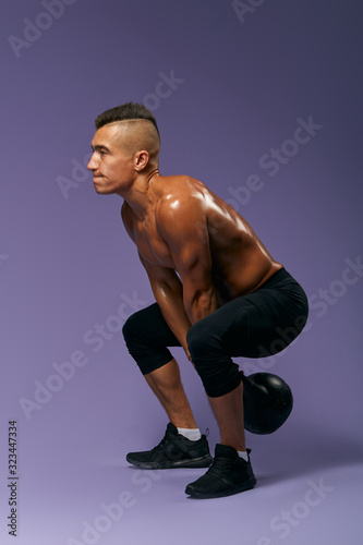 Fit serious hardworking man doing squats, isolated over a gray background, full length side view photo. strength training, motivation