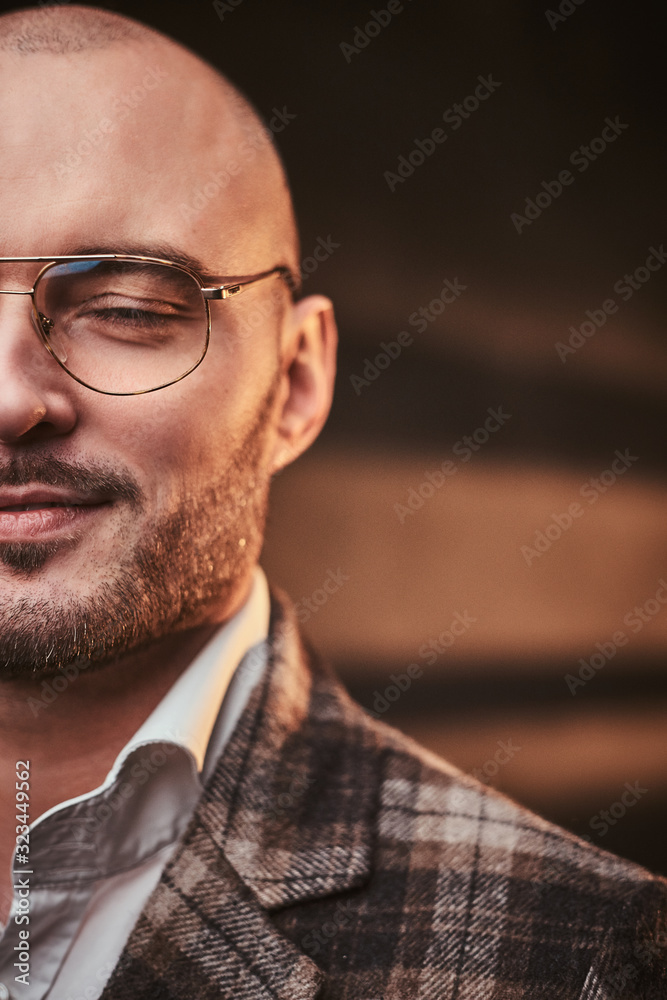 Obraz premium Fashionable and calm bald businessman posing with closed eyes for camera in a studio wearing chic checkered wool jacket, white shirt and glasses