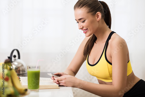 Sporty girl texting on cellphone and drinking detox smoothie