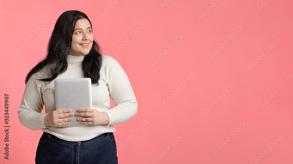 Smiling plus sized girl holding digital tablet and looking aside Smiling plus sized girl holding digital tablet and looking aside