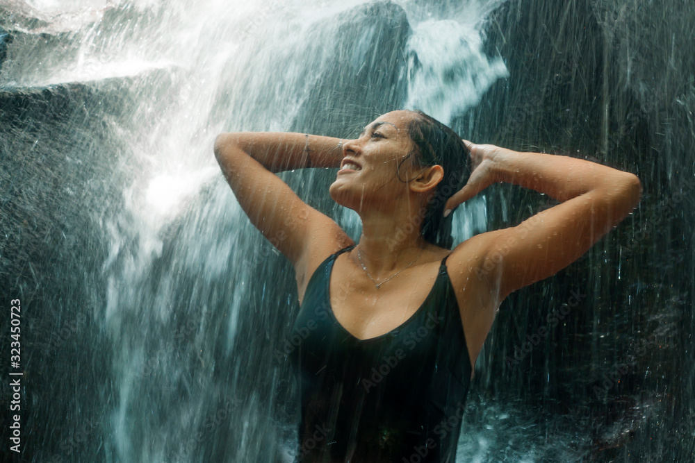 Fototapeta premium young attractive and blissful Asian Indonesian woman overwhelmed by the beauty of natural waterfall in tropical jungle enjoying happy the amazing and exotic travel destination