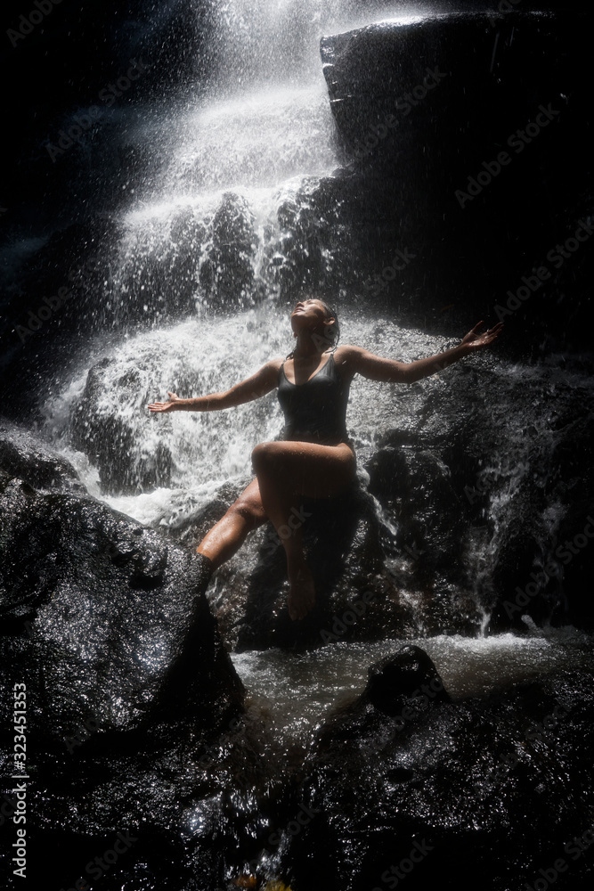 Obraz premium young attractive and blissful Asian Indonesian woman overwhelmed by the beauty of natural waterfall in tropical jungle enjoying happy the amazing and exotic travel destination