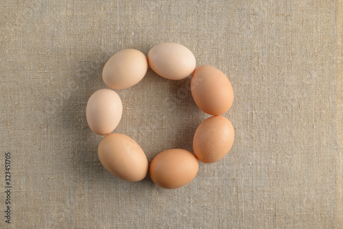 Seven fresh brown chicken eggs in shape of a circle on a canvas background. Healthy good nutrition. Natural organic farm products.