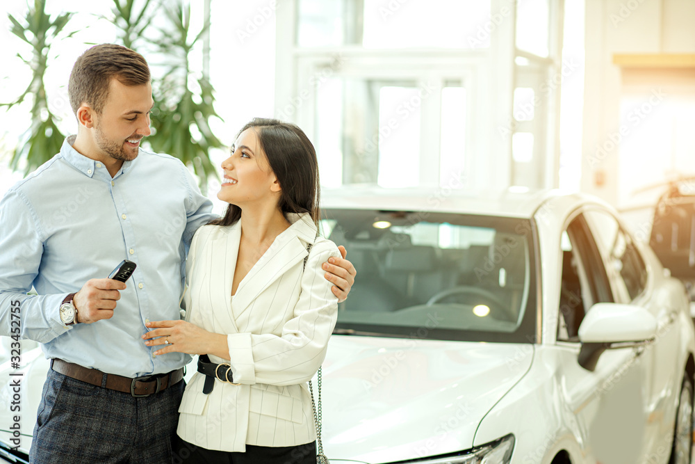 new young owners of beautiful car in showroom, attactive lady and handsome man came in dealership to get new automobile, they happily hold keys from it new young owners of beautiful car in showroom, attactive lady and handsome man came in dealership to get new automobile, they happily hold keys from it