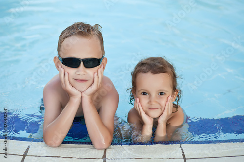 Happy boy with blond hair and little girl smiling sitting in swimming pool.