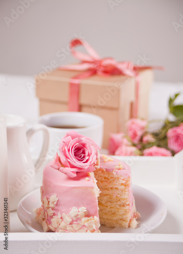 Mini small cake with pink glaze, beautiful roses, cup of coffee, gift box on the white table.