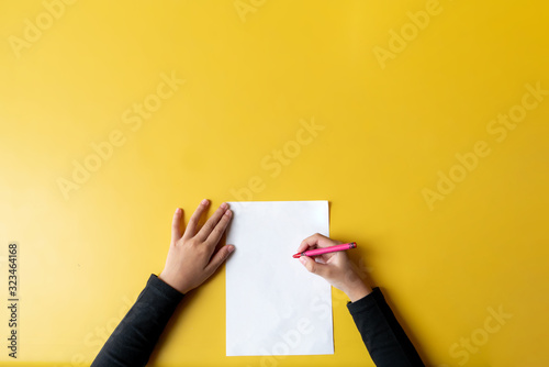 Top view of child hand and blank paper with color pencil on yellow table