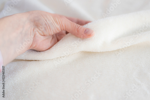 Female hand touches soft cozy plaid of white fabric with a pile. Textile material, pleasant to the touch