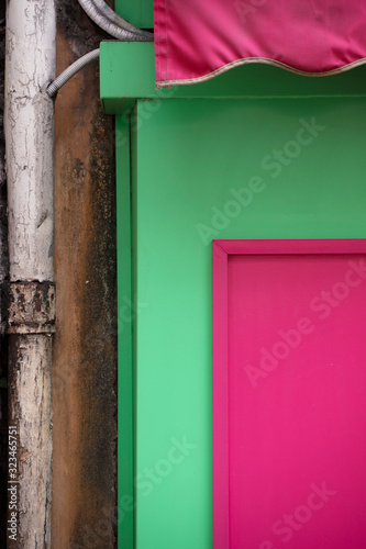 Boutique à la façade coffrée de bois peint vert et rose d'un vieil immeuble vétuste à la tuyauterie endommagée.