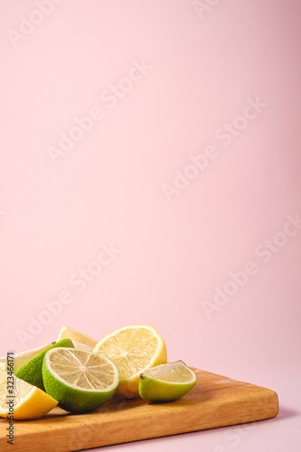 Fresh tasty lemon and lime citrus fruits slices on wooden cutting board, minimal pink background isolated, angle view