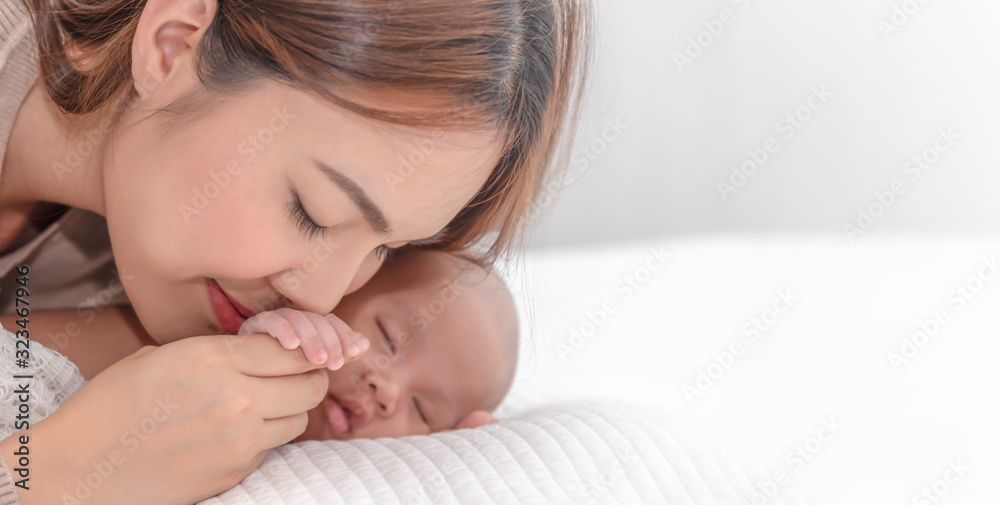 Close up beautiful young asian mother kissing her newborn one month baby sleep in bed. Healthcare and medical love asia woman lifestyle mother's day concept. Close up beautiful young asian mother kissing her newborn one month baby sleep in bed. Healthcare and medical love asia woman lifestyle mother's day concept.