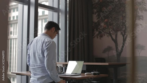 asian man works on laptop stand desk behind angle
