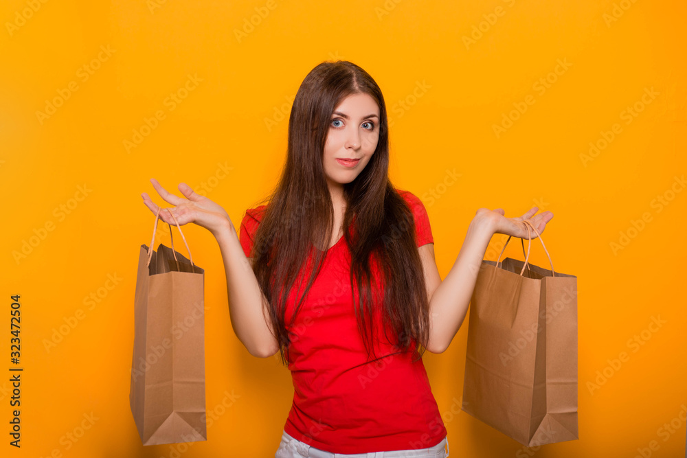Portrait of a cheerful, happy, young woman with paper bags in hands standing on a yellow background. Shopping, discount day, black friday. Portrait of a cheerful, happy, young woman with paper bags in hands standing on a yellow background. Shopping, discount day, black friday.