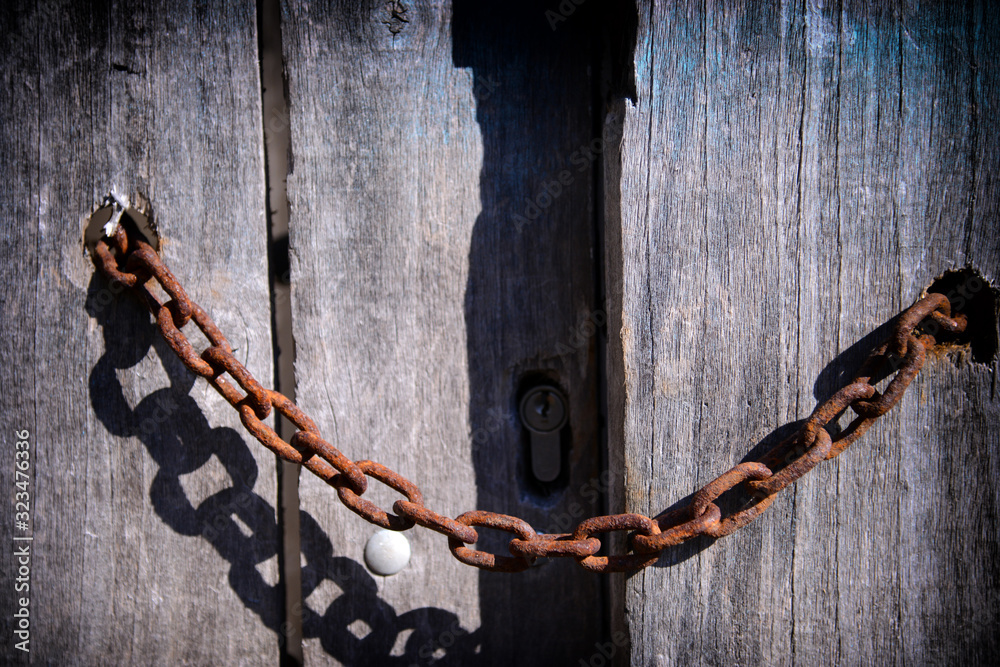 Old wooden door secured by a rusty chain Old wooden door secured by a rusty chain