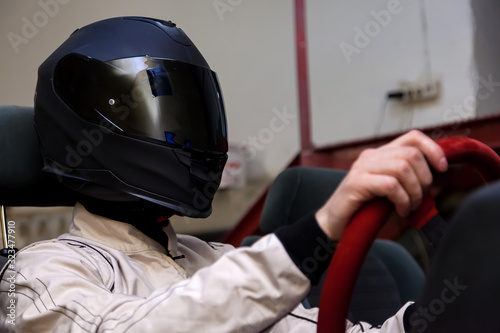 A professional racer in a black helmet and a white homologated suit sits in the sports seat of a car for drifting and racing during a race and training on a simulator. photo