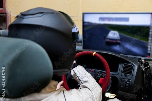 A professional racer in a black helmet and a white homologated suit sits in the sports seat of a car for drifting and racing during a race and training on a simulator. photo