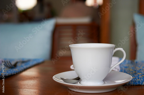 White cup of tea or hot coffee with spoon on blur table dining background
