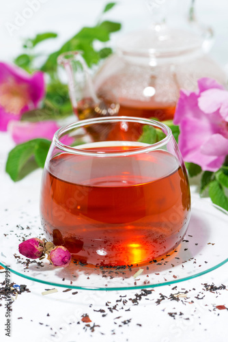 fragrant tea with wild rose in a glass cup on a white table, vertical closeup