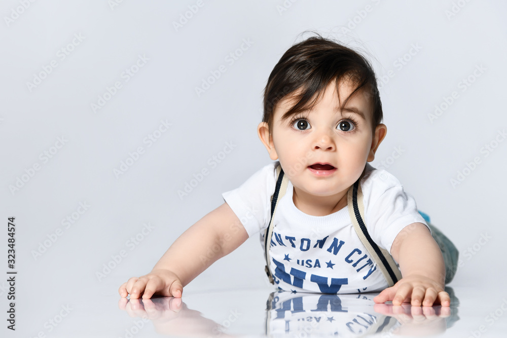 Little toddler in t-shirt with inscriptions, jeans with suspenders. He is laying on floor isolated on white background. Close up Little toddler in t-shirt with inscriptions, jeans with suspenders. He is laying on floor isolated on white background. Close up