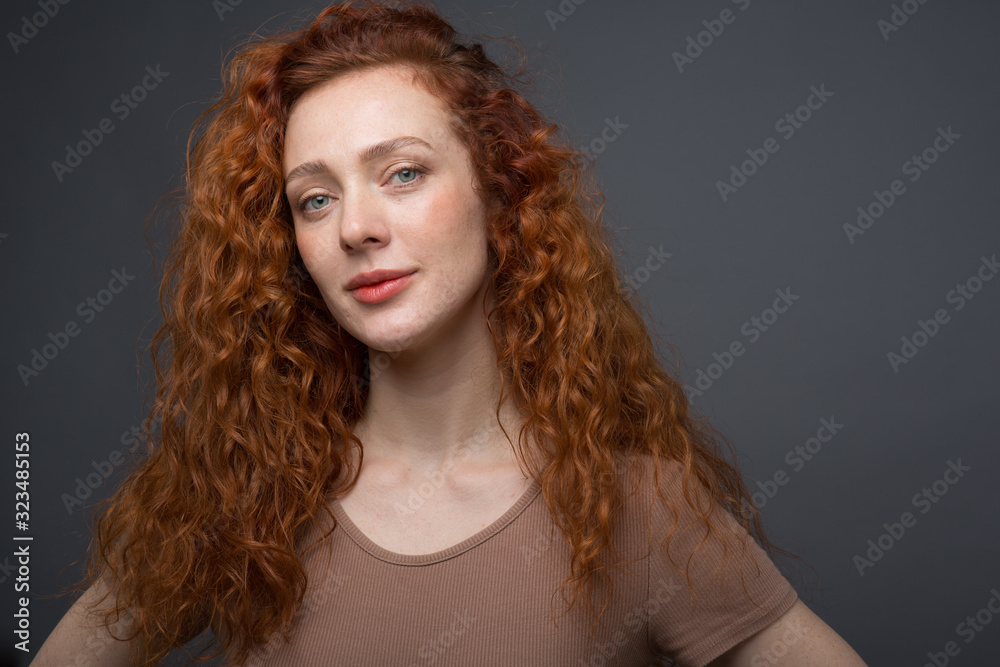 Happy curly red-haired woman with a beautiful smile, looking directly at the camera. On an isolated gray background. The concept of happiness and emotions Happy curly red-haired woman with a beautiful smile, looking directly at the camera. On an isolated gray background. The concept of happiness and emotions