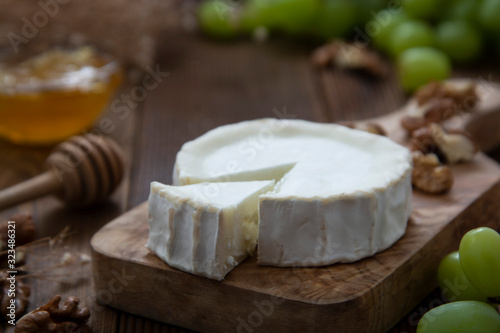 White, round cheeses on wooden background with honey and grapes. Dark food photo.