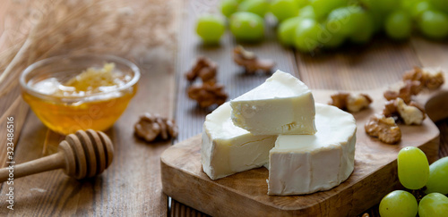 White, round cheeses on wooden background with honey, nuts and grapes. Dark food photo banner.