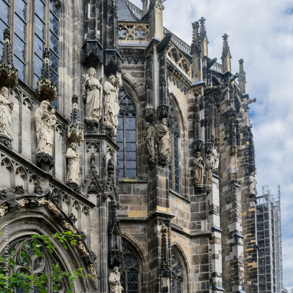Detail of medieval Aachen Cathedral exterior in Aachen Germany in brown and ochre colors, featuring cathedral walls with Gothic windows, towers, sculptures and ornaments.
