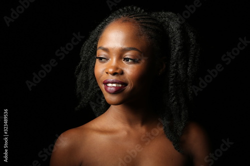 Portrait of a young beautiful African woman with thick black curly hair on an isolated black background. The woman smiles