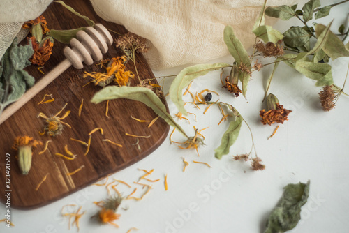 Brewed herbal tea in glass cups on a white background, with ranner and a wooden board. Herbal tea ingredients on a black background. Dried mint, blueberries, linden flowers, Merigold flower, Calendula