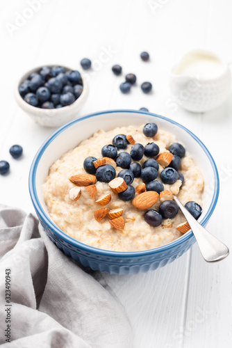 Bowl of porridge oats with blueberries, almonds on white wooden table background. Healthy breakfast, clean eating concept