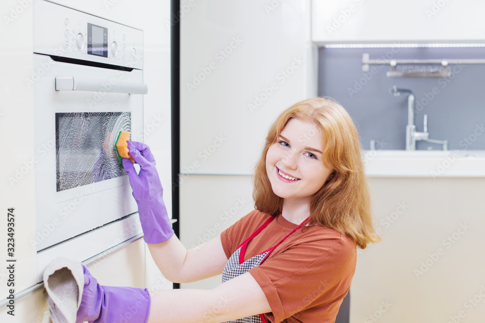 girl in purple gloves sponges oven in  modern kitchen