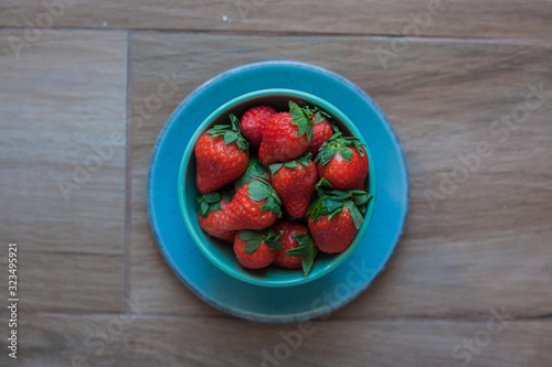 Strawberries in a mint green bowl on a blue plate with rustic wooden background