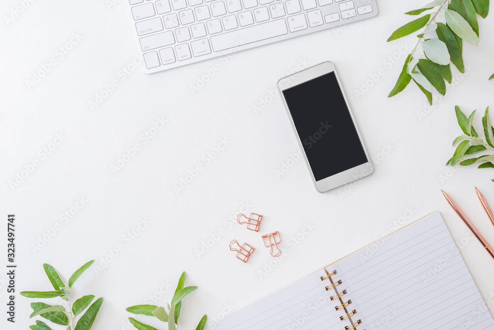 Flat lay home office desktop with keyboard, smartphone, notebook and green leaves on a white background Flat lay home office desktop with keyboard, smartphone, notebook and green leaves on a white background