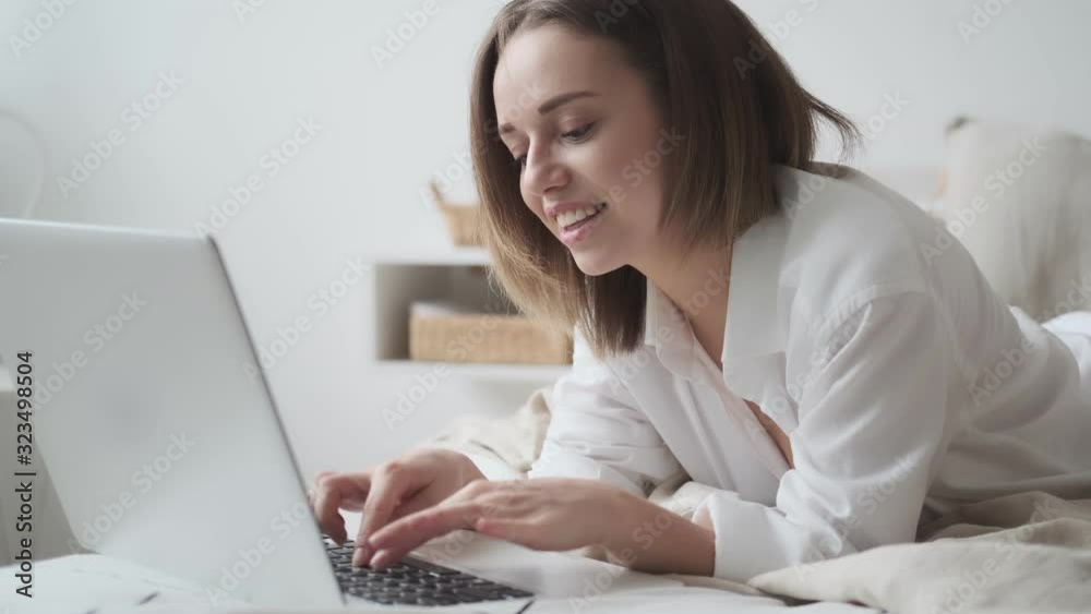 young woman uses a laptop while lying in bed. girl working on a laptop in the morning, comfortably sitting in bed young woman uses a laptop while lying in bed. girl working on a laptop in the morning, comfortably sitting in bed
