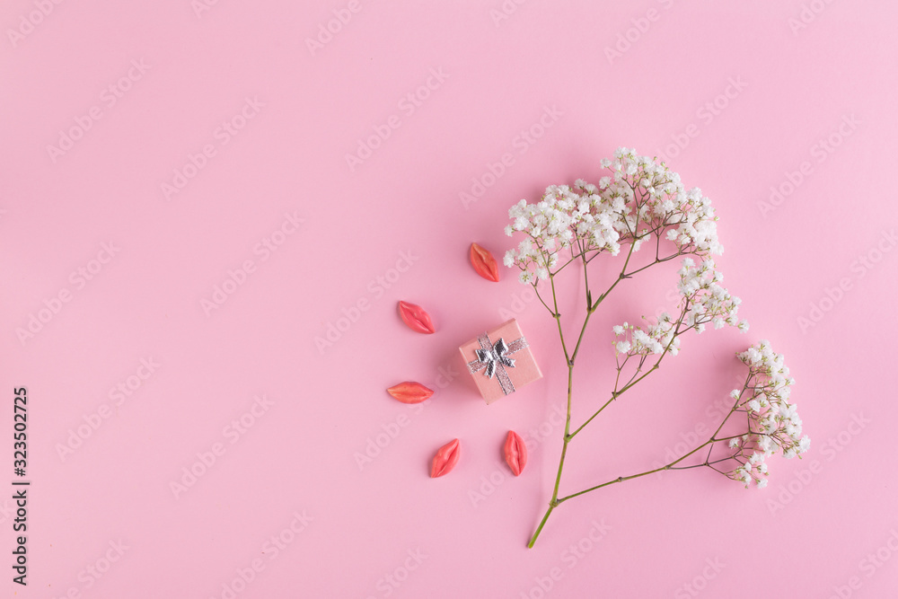 A branch of white small flowers and a small gift box on a pink paper background.