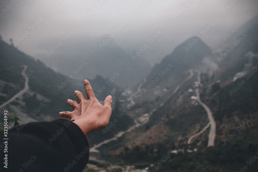 A hand reaching out to the foggy mountains and winding roads of Ha giang Loop in Vietnam showing a cinematic and moody travel photo