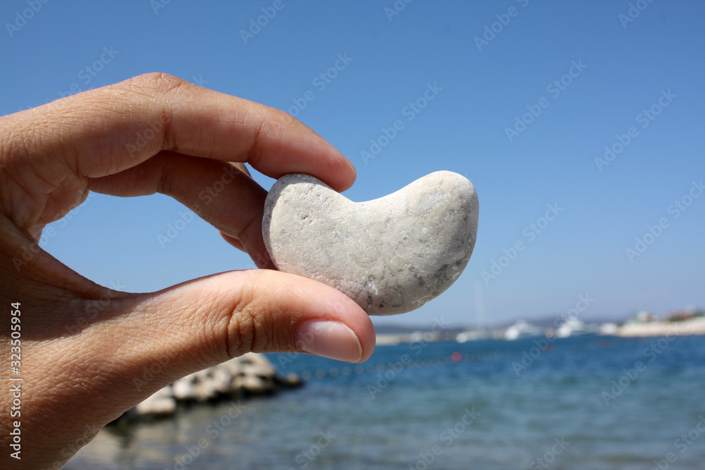 Stone in heart shape in the hand on the beach landscape