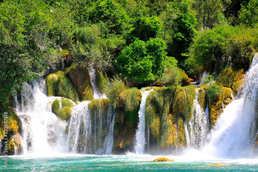 A picturesque waterfall among large stones in the Krka waterfalls, Lakes Landscape Park, Croatia in spring or summer. Croatian waterfalls, mountains and nature. A picturesque waterfall among large stones in the Krka waterfalls, Lakes Landscape Park, Croatia in spring or summer. Croatian waterfalls, mountains and nature.