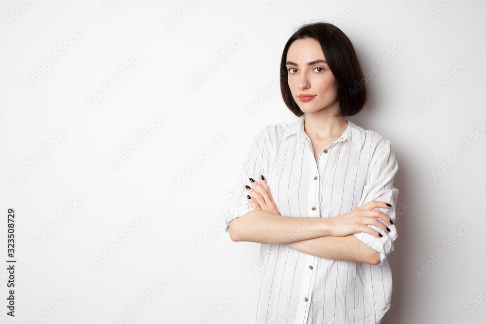 Beautiful looking at the camera with folded arms. Portrait of a cute girl in a white shirt on a white background. Beautiful looking at the camera with folded arms. Portrait of a cute girl in a white shirt on a white background.