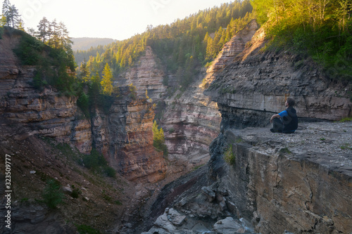 Panoramic view of young hiker standing on a cliff in scenic Bletterbach gorge in South Tyrol enjoying the view on a beautiful sunny day with blue sky on golden hour , Alto Adige, ITALY