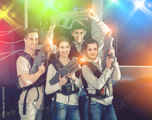 Happy young people with laser pistols posing together in bright beams in laser tag labyrinth
