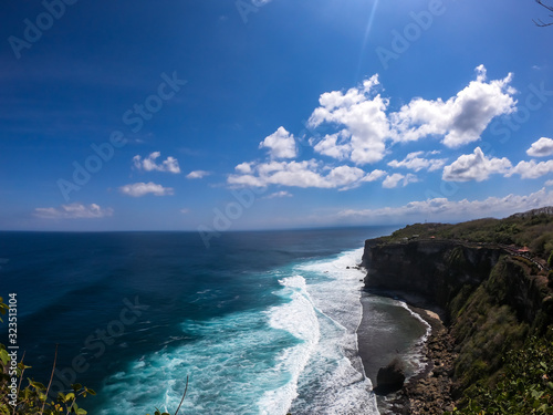 A done shot of Uluwatu Cliffs, Bali, Indonesia. The waves are rushing to the shore, making the water bubbly. The beach is covered with green algae, further on it's sandy. Hidden gem of Indonesia. © Chris