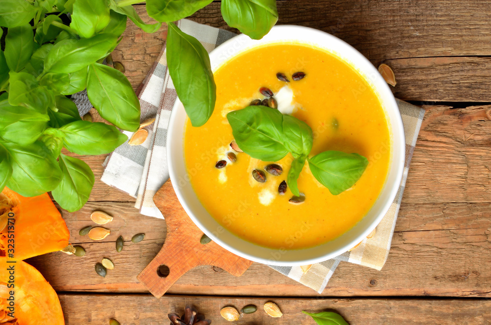 Bowl of cream pumpkin, carrot soup with fresh basil, pumpkin seed on rustic wooden table. Top view. Bowl of cream pumpkin, carrot soup with fresh basil, pumpkin seed on rustic wooden table. Top view.