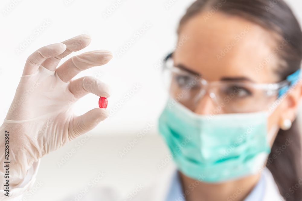 Young female scientist holding a red pill - close-up Young female scientist holding a red pill - close-up