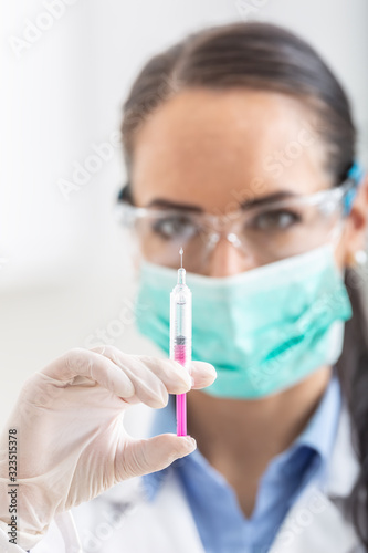 Female doctor working with syringe needle and ampoule of medicine. A scientist in sterile clothes is making a vaccine drug © weyo