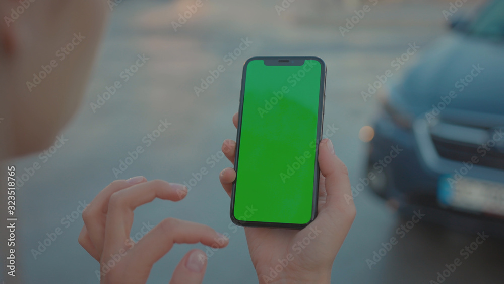 Lviv, Ukraine - May 19, 2018: Young woman hitchhiking on night highway holding and using modern mock-up vertical smartphone greenscreen outdoors. Close-up. Lviv, Ukraine - May 19, 2018: Young woman hitchhiking on night highway holding and using modern mock-up vertical smartphone greenscreen outdoors. Close-up.