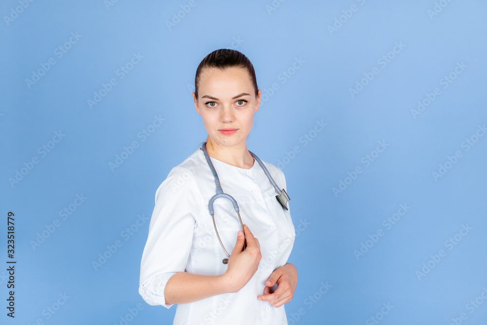 Medical concept of beautiful female doctor in white coat with phonendoscope. Medical student general practitioner. Woman hospital worker looking at camera and smiling, studio, blue background. Medical concept of beautiful female doctor in white coat with phonendoscope. Medical student general practitioner. Woman hospital worker looking at camera and smiling, studio, blue background.
