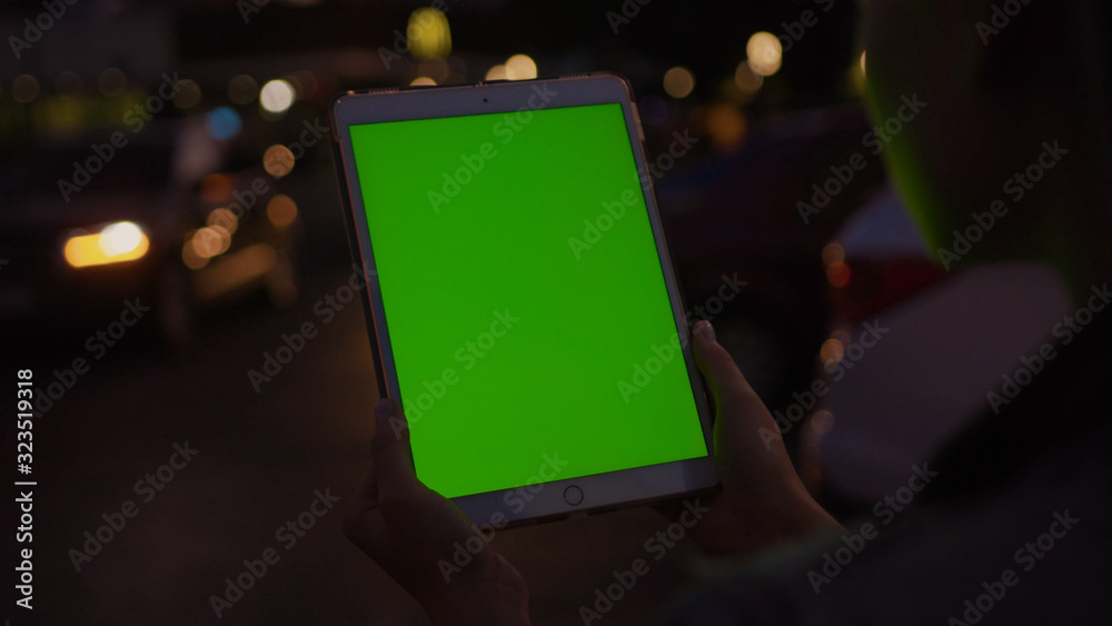 Lviv, Ukraine - May 19, 2018: Close-up of girl holding vertical tablet digital computer with mock-up green display in busy city road during night time. Urban lifestyle. Lviv, Ukraine - May 19, 2018: Close-up of girl holding vertical tablet digital computer with mock-up green display in busy city road during night time. Urban lifestyle.